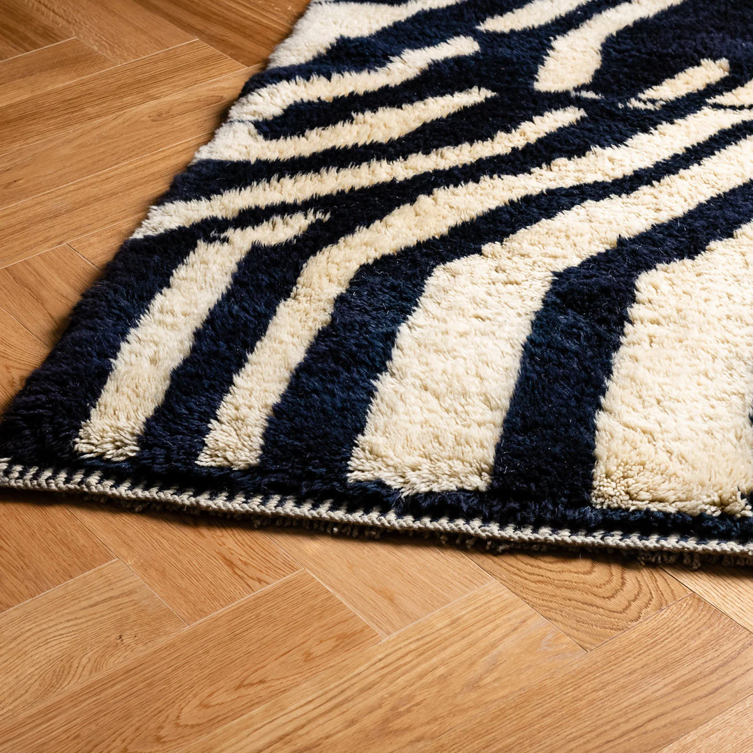 Abstract Beni Mrirt wool rug with black and white design on wooden floor. Moroccan berber carpet for modern home decor.