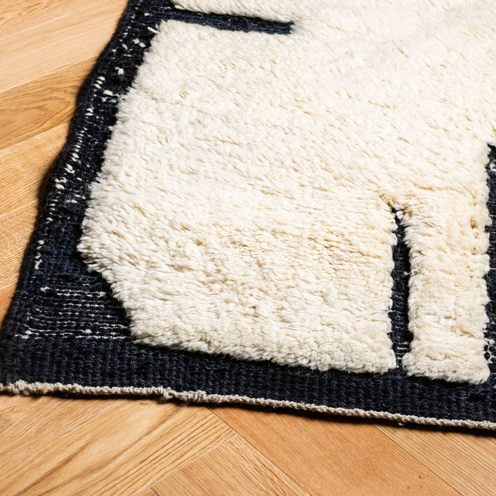 Close-up of abstract cream and black handmade Moroccan wool rug detail on wood floor, showcasing texture and craftsmanship.