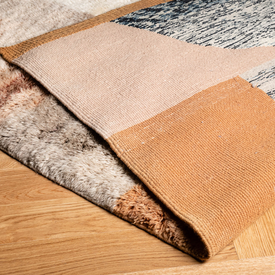 Abstract Moroccan wool rug with earthy tones and high-pile texture, blending traditional and modern boho design on a wooden floor.