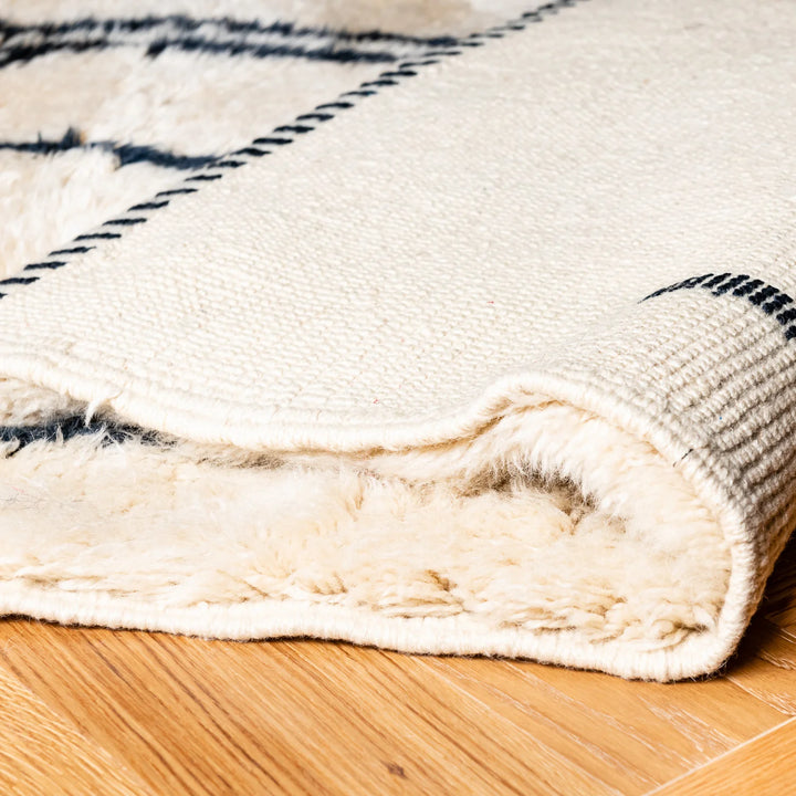 Close-up of an ivory Moroccan wool rug with black tribal patterns, showcasing plush texture and premium craftsmanship.