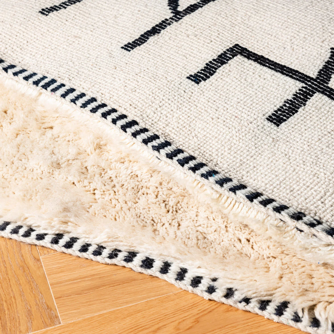 Close-up of an Abstract Tribal Beni Mrirt Rug showcasing handwoven Moroccan wool with black geometric patterns on ivory background.