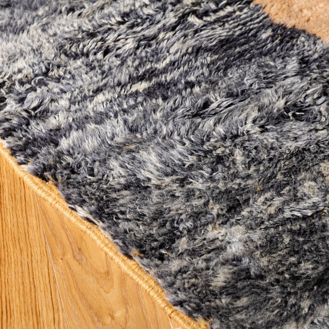Close-up of textured Moroccan wool rug with charcoal and ivory tones on a hardwood floor, highlighting its plush, hand-knotted design.