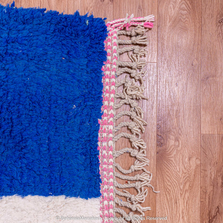 Close-up of a handmade Moroccan wool rug with blue and pink fringe, showcasing traditional craftsmanship and vibrant colors.