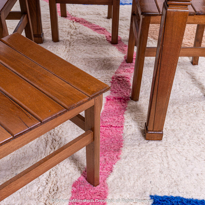 Handmade Moroccan wool rug with abstract design, featuring pink and blue accents under wooden furniture.