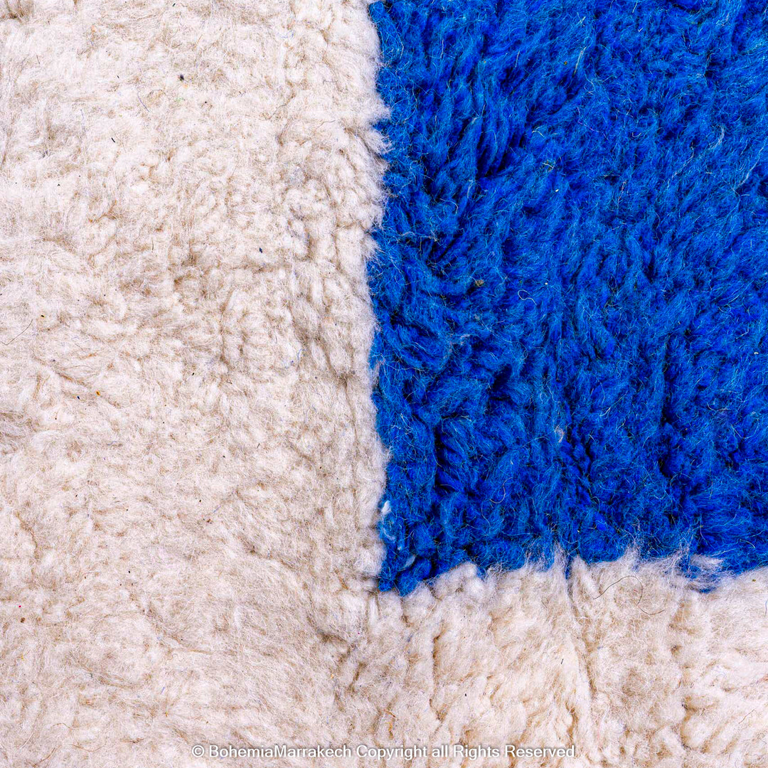 Close-up of handmade Moroccan wool shag rug with abstract blue shape and ivory base.