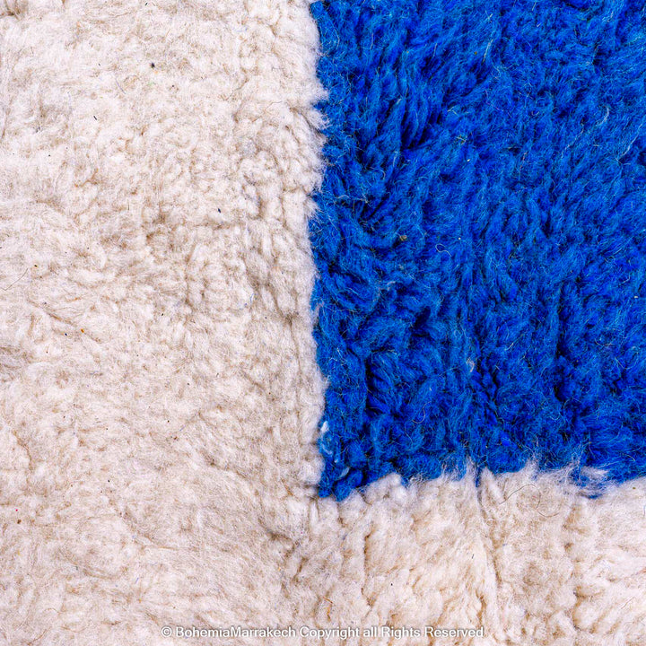 Close-up of handmade Moroccan wool shag rug with abstract blue shape and ivory base.