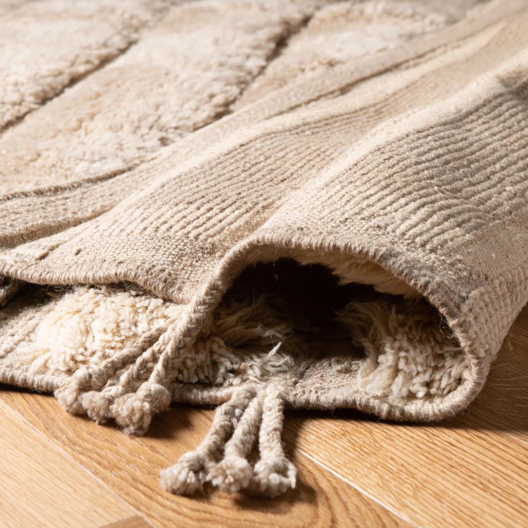 Handwoven beige Moroccan wool rug on wooden floor, showcasing Berber shag style and intricate detail, ideal for modern home decor.