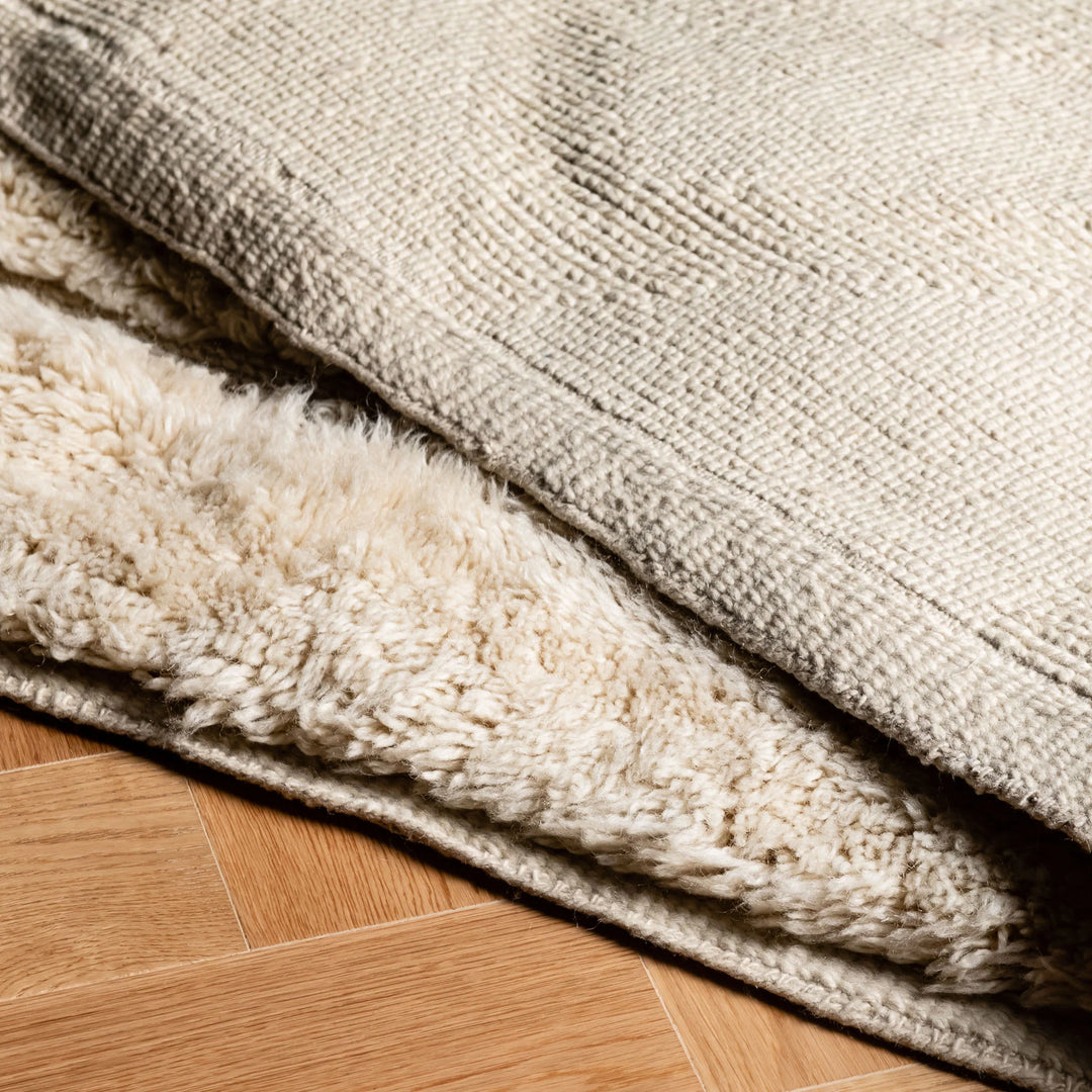 Beige Moroccan wool rug with minimalist triangle design, handcrafted in the Atlas Mountains. Luxurious soft texture on wood floor.