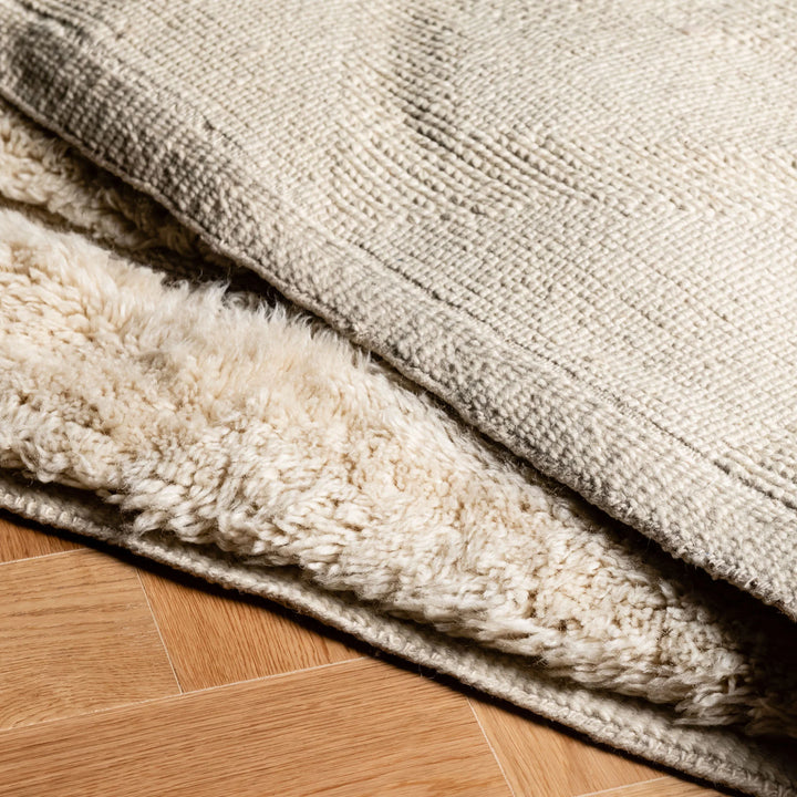 Beige Moroccan wool rug with minimalist triangle design, handcrafted in the Atlas Mountains. Luxurious soft texture on wood floor.