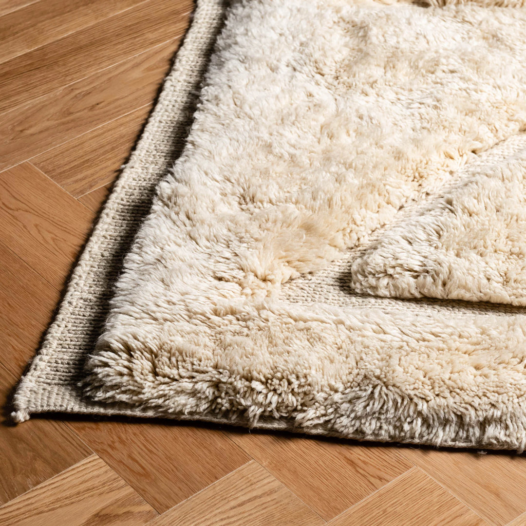 Beige Moroccan wool rug with minimalist triangle design on wooden floor, showcasing plush texture and artisanal craftsmanship.