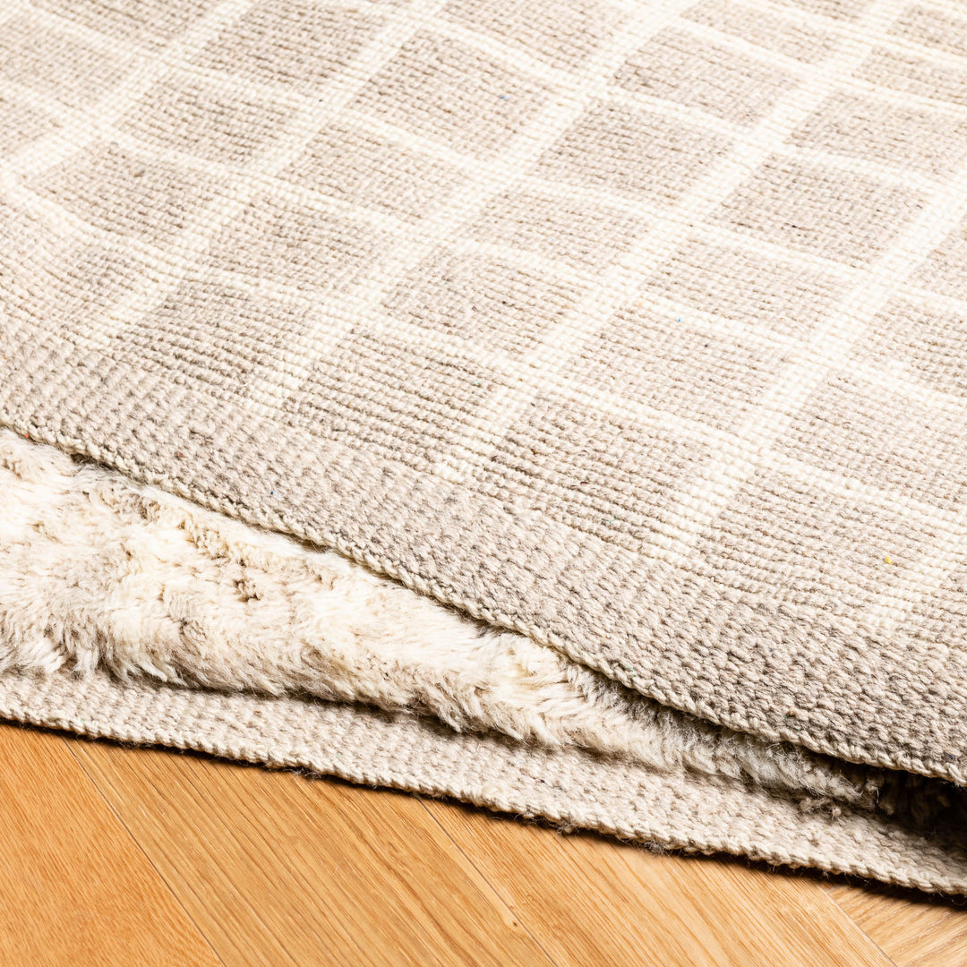 Beige Moroccan wool rug with subtle grid pattern on wooden floor, handmade traditional Berber style, perfect for modern interiors.
