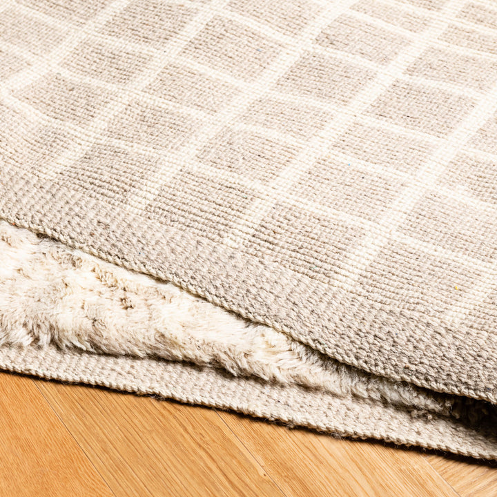 Beige Moroccan wool rug with subtle grid pattern on wooden floor, handmade traditional Berber style, perfect for modern interiors.