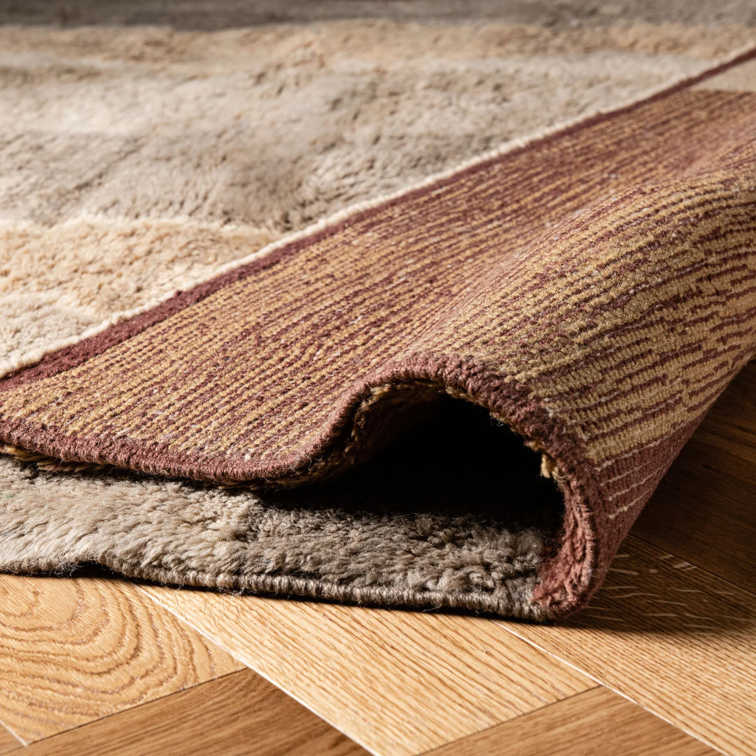 Close-up of a folded Beni Mrirt Moroccan wool rug with earthy geometric design on wooden floor.