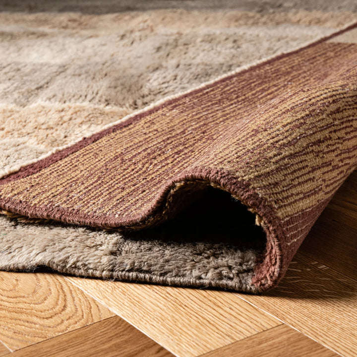 Close-up of a folded Beni Mrirt Moroccan wool rug with earthy geometric design on wooden floor.