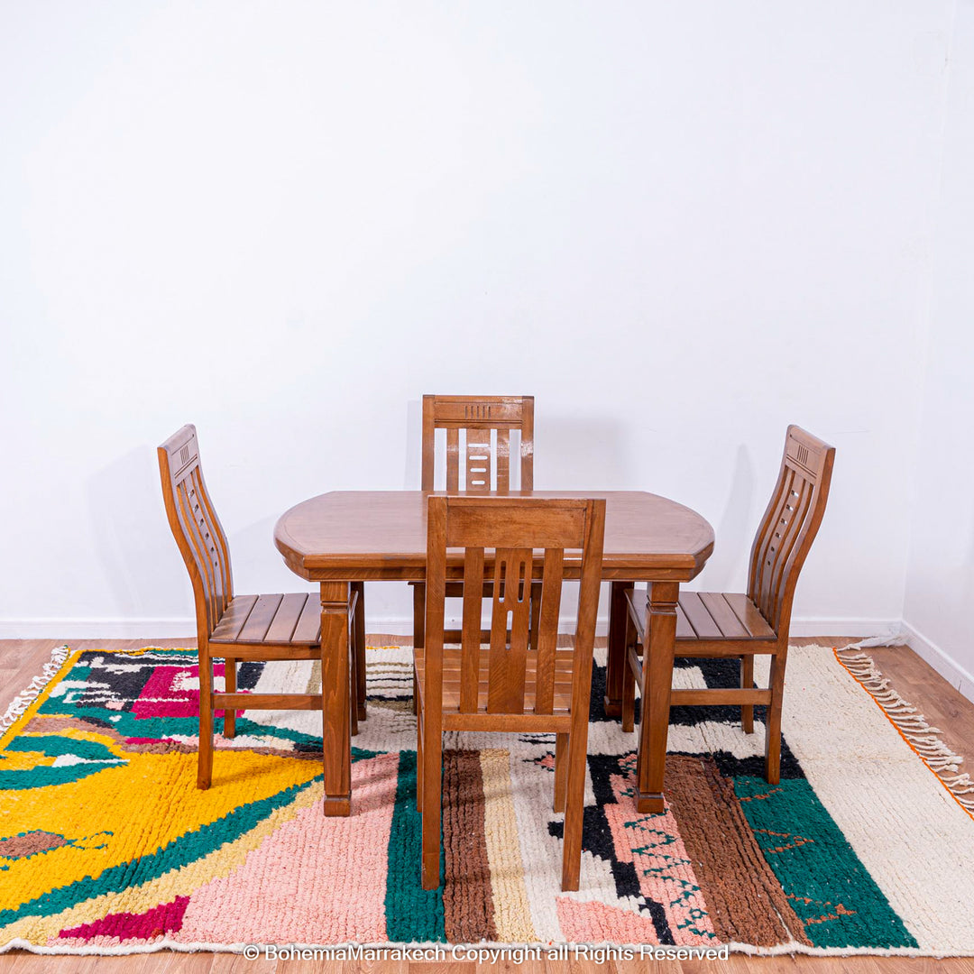 Dining set on colorful Moroccan wool rug with geometric patterns in green, pink, and yellow, adding warmth and style to the room.