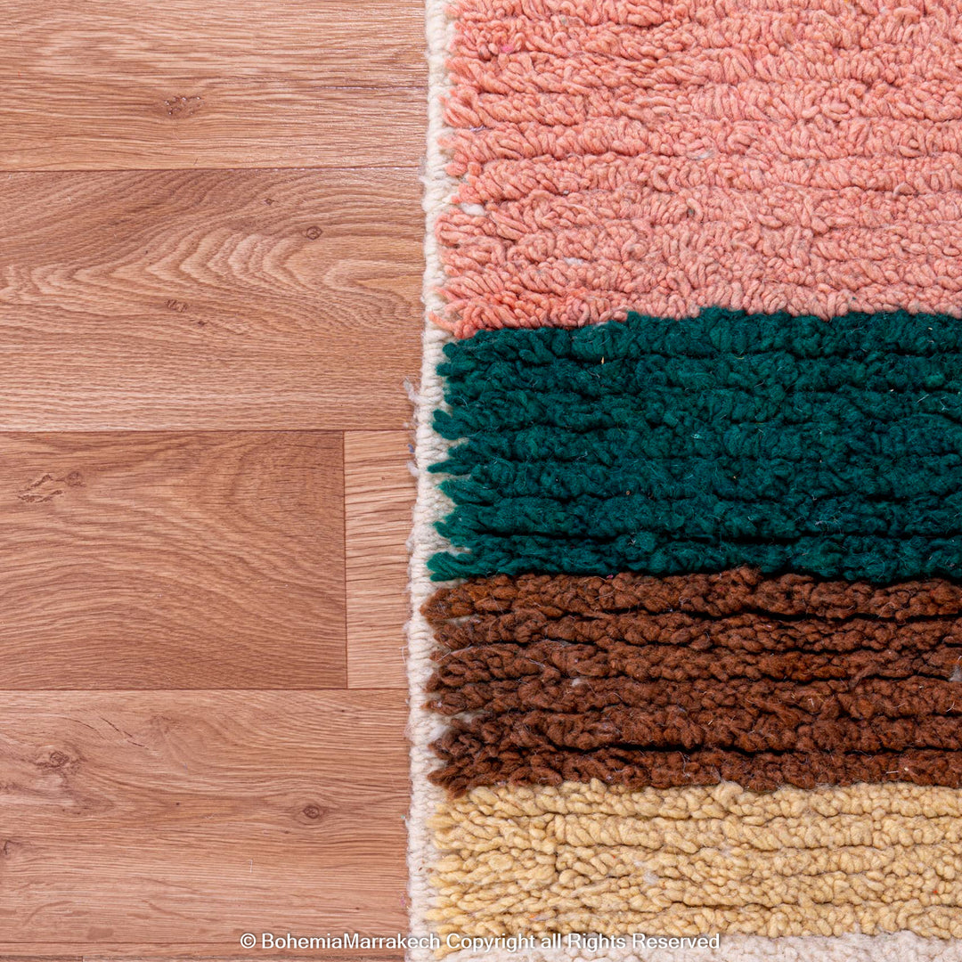 Handmade Moroccan shag rug with pink, green, brown, and yellow geometric patterns on wooden floor