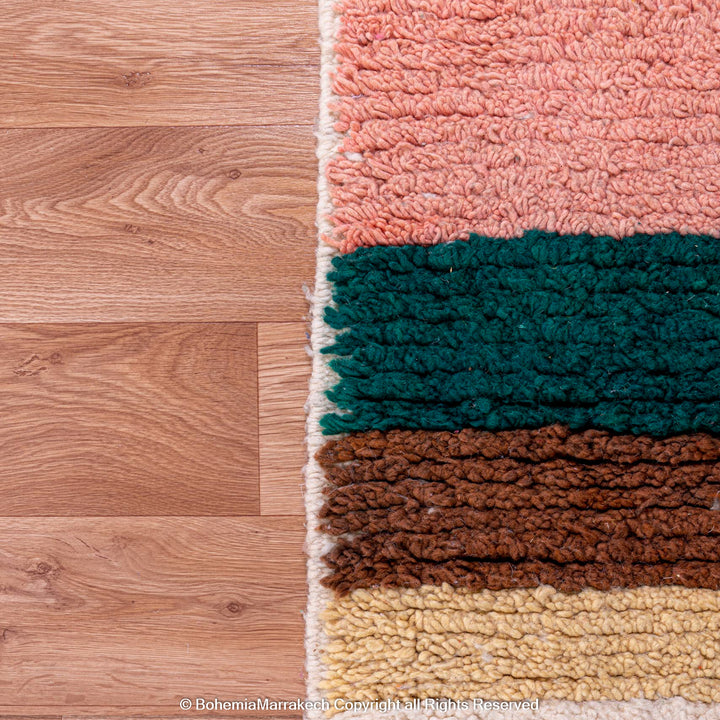 Handmade Moroccan shag rug with pink, green, brown, and yellow geometric patterns on wooden floor