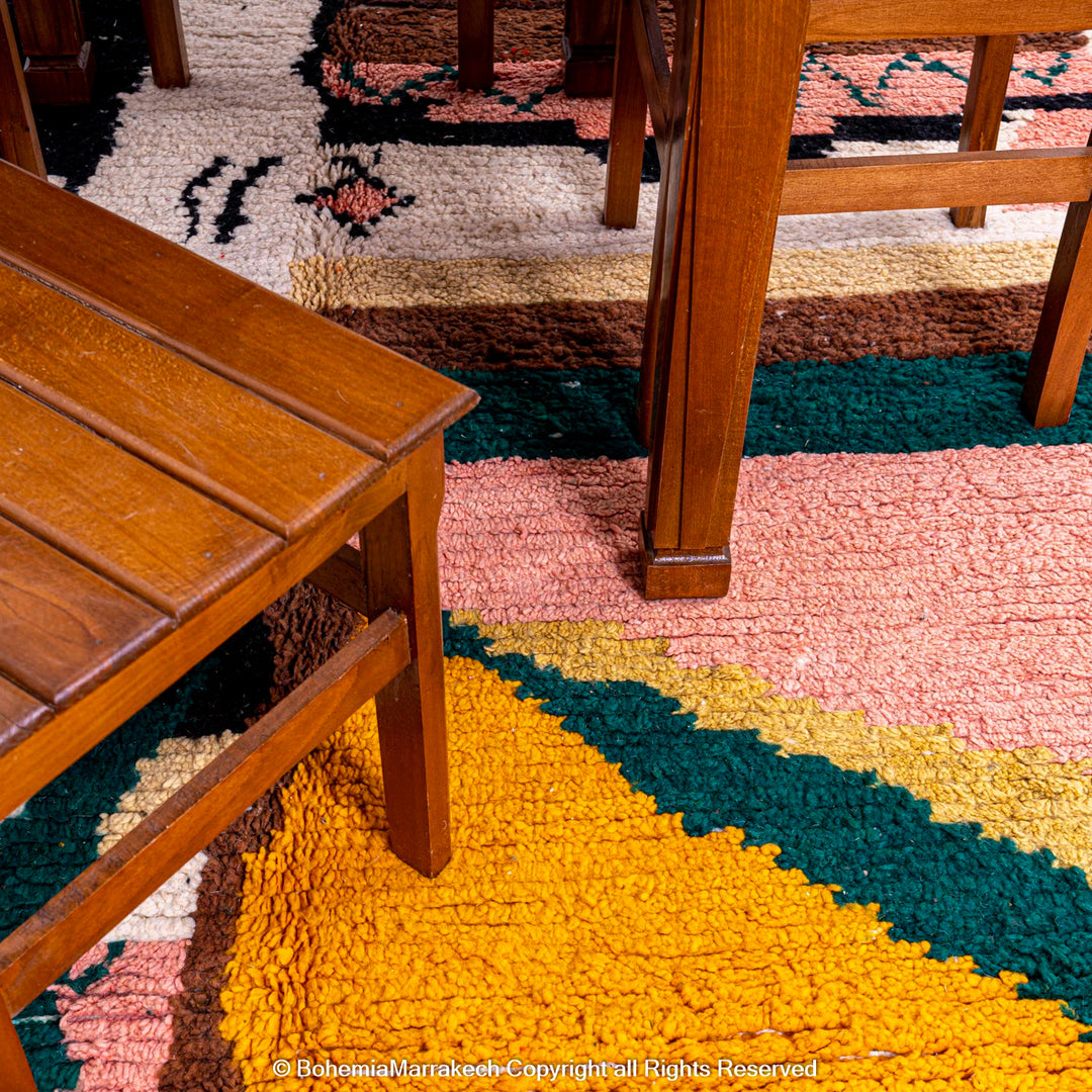 Custom Beni Ourain Moroccan wool rug with vibrant geometric patterns in pink, green, and yellow under wooden furniture.