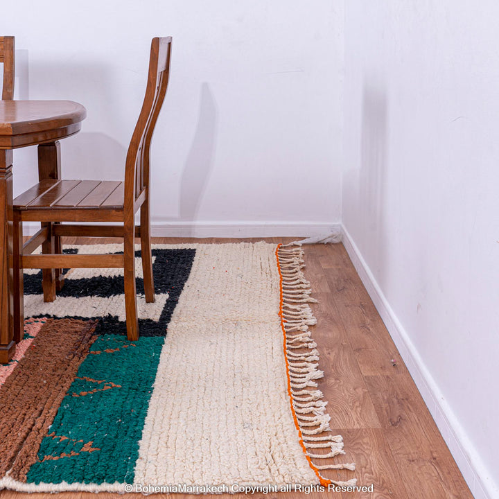Custom Beni Ourain Moroccan rug with geometric patterns in earthy tones lies beside a wooden dining table and chairs.