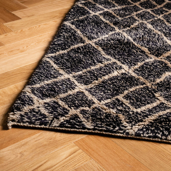 Close-up of black diamond pattern Beni Mrirt Moroccan rug with beige grid, handwoven wool, on wooden floor