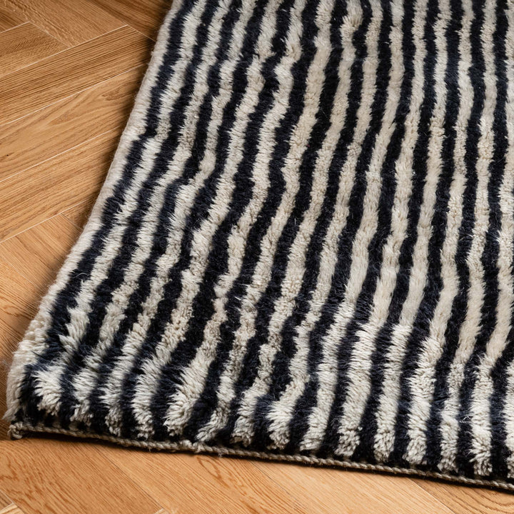 Black and ivory stripe handmade Moroccan wool rug on wooden floor, ideal for modern interiors. Moroccan rugs for sale.