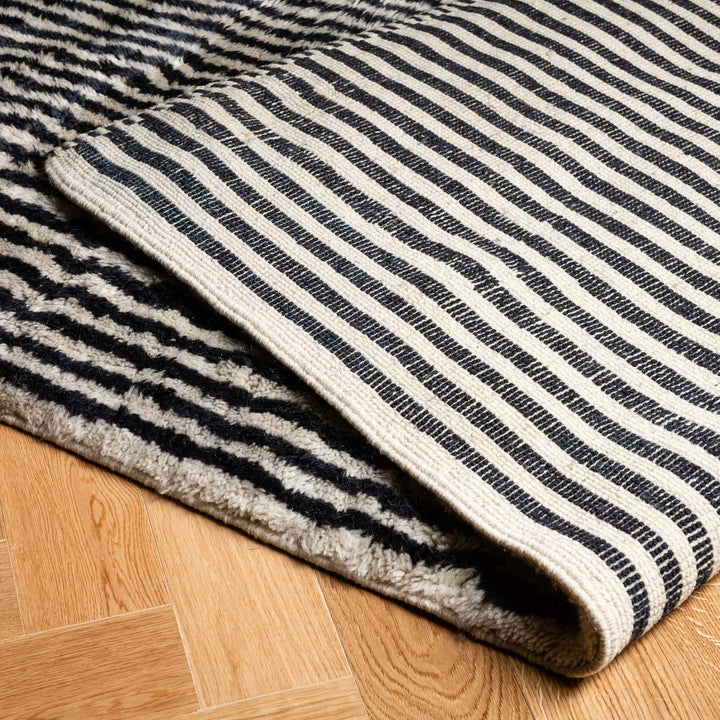Handmade Moroccan rug with black and ivory stripes, crafted from wool, ideal for modern interiors, shown on hardwood floor.