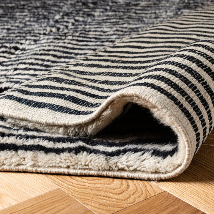 Black and ivory stripe Moroccan wool rug, handmade and folded, showcasing texture on wooden floor. Perfect for modern interiors.