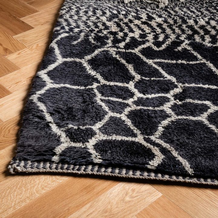 Black and white handmade Moroccan wool rug with abstract geometric design on hardwood floor.