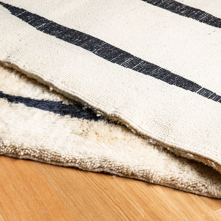 Black and white Moroccan wool rug with vertical stripes, handcrafted Berber style, showcasing soft texture. Perfect for modern interiors.
