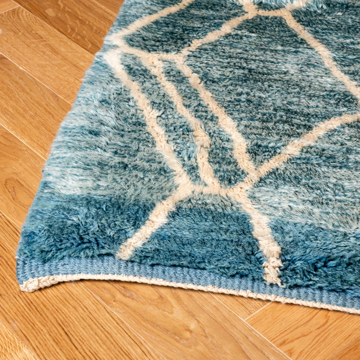 Blue Moroccan wool rug with ivory diamond pattern on wooden floor, showcasing plush texture and gradient hues.