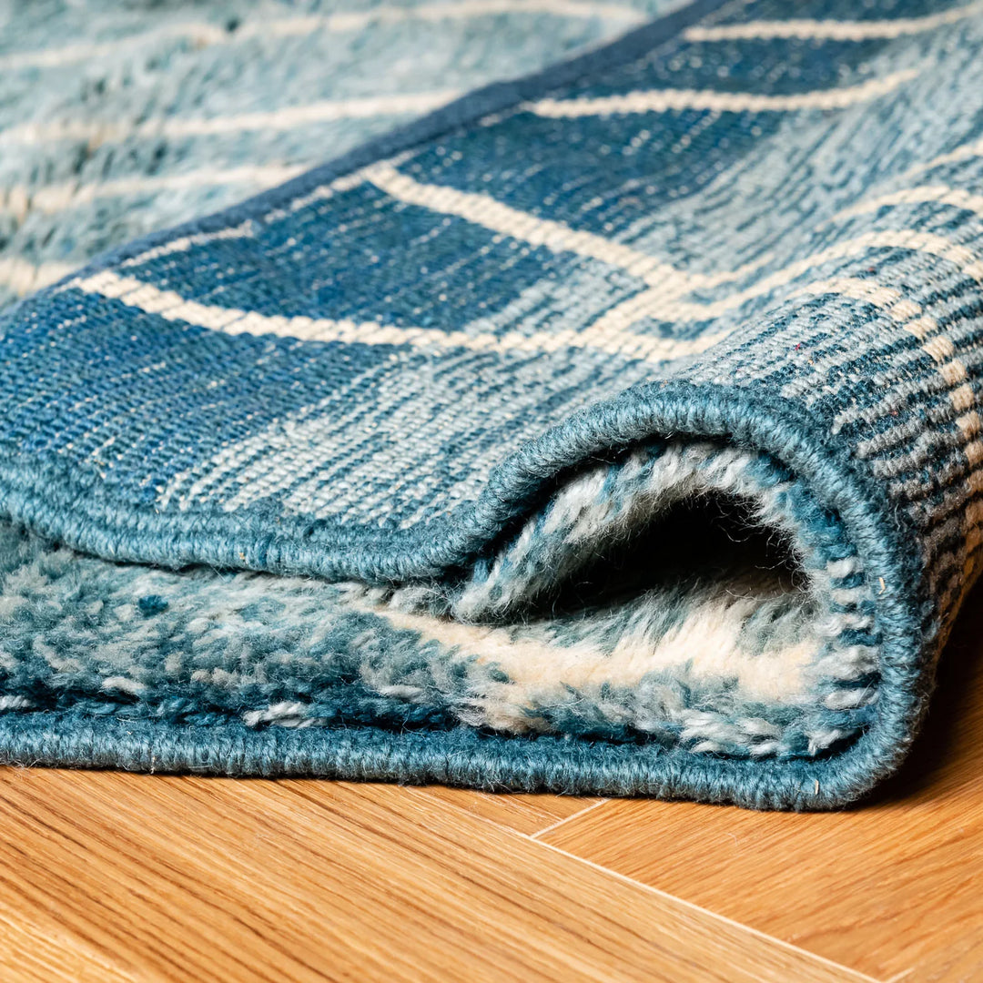 Close-up of blue Moroccan wool rug with geometric diamond pattern, showcasing plush texture and durable quality on wood floor.