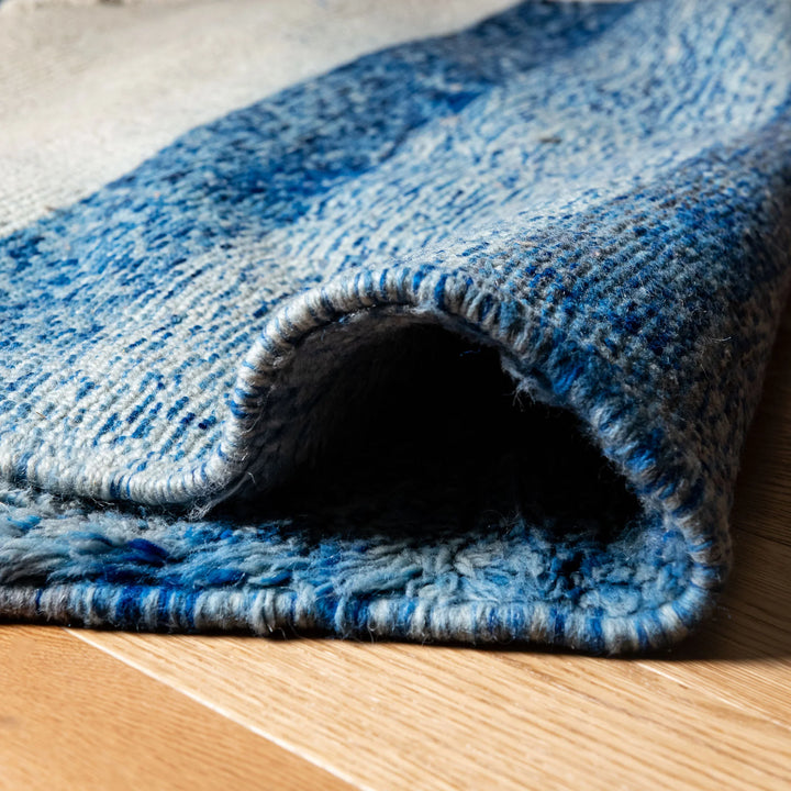 Close-up of blue and white handmade Moroccan rug in natural wool with abstract patterns, showcasing texture and color detail.