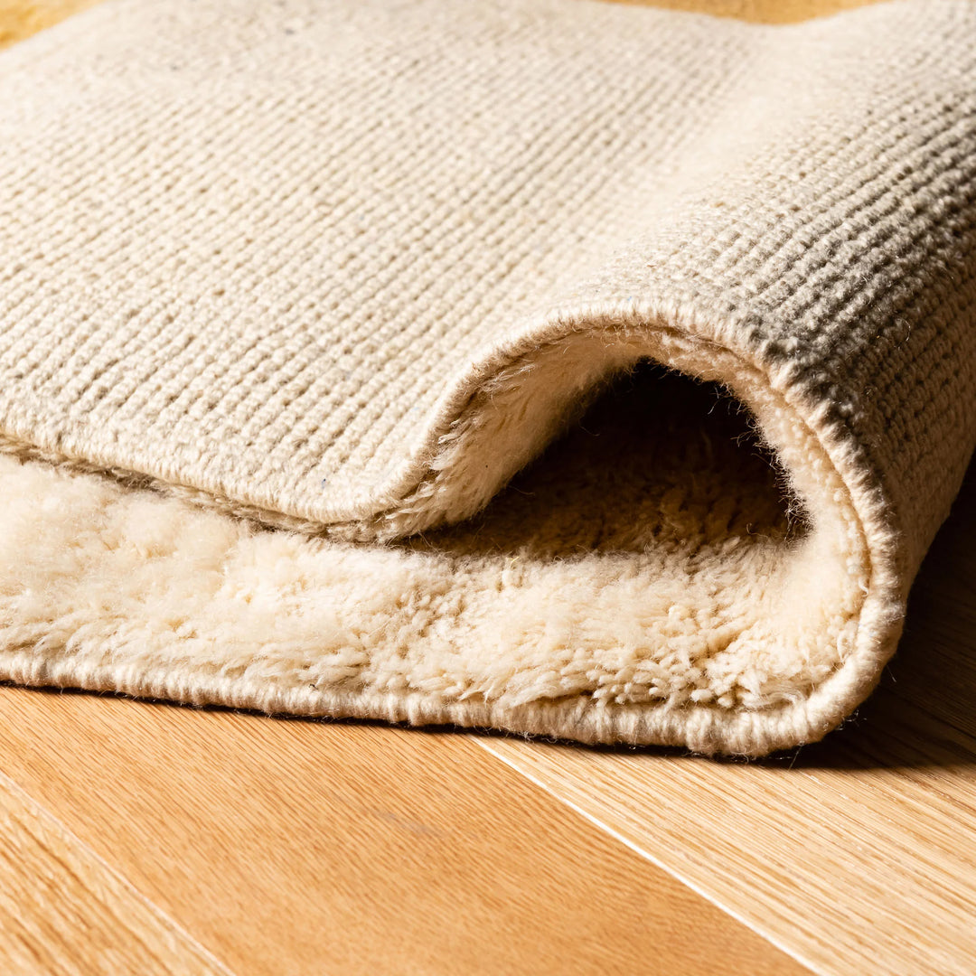 Close-up of luxurious Moroccan wool rug with creamy woven texture, showcasing plush and soft underfoot feel, handcrafted by skilled artisans.