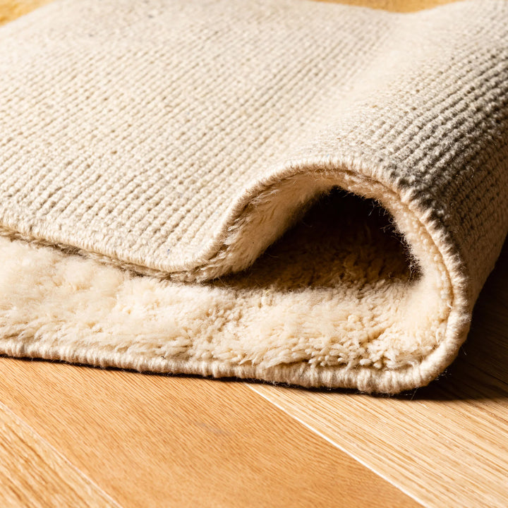 Close-up of luxurious Moroccan wool rug with creamy woven texture, showcasing plush and soft underfoot feel, handcrafted by skilled artisans.