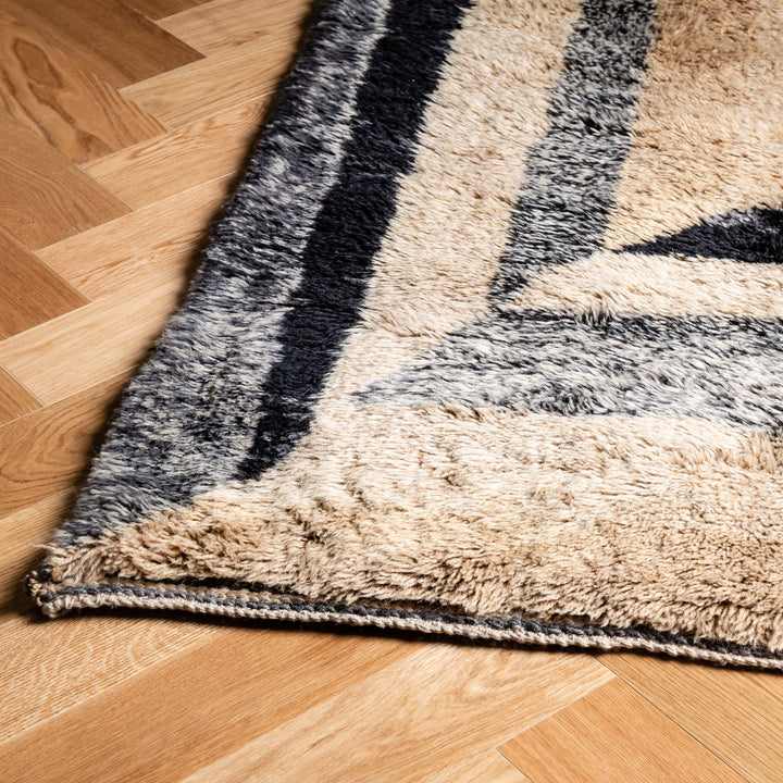 Black beige handwoven geometric Moroccan wool rug on wooden floor, modern Beni Mrirt style, cozy and elegant flooring option.