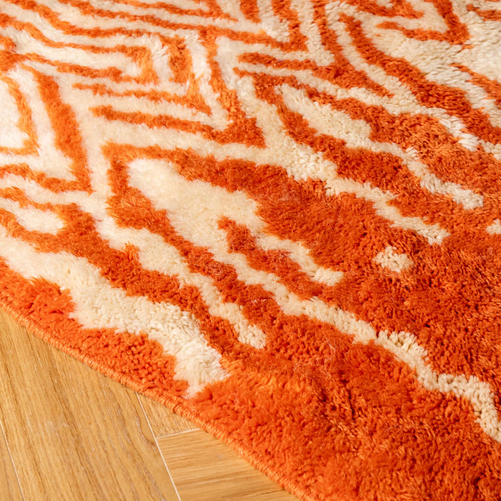 Bold orange Moroccan rug with tribal zigzag pattern on a wooden floor, showcasing vibrant Berber weaving techniques.