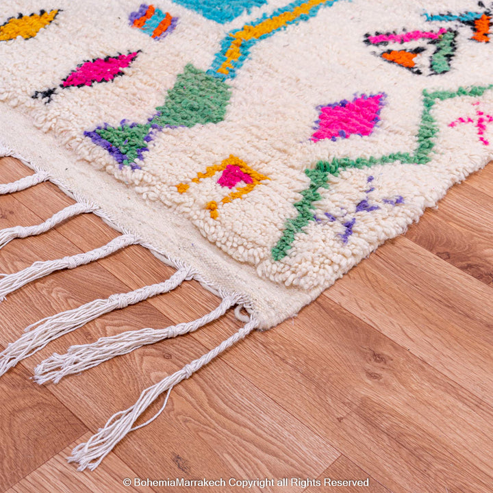 Colorful Azilal Moroccan Berber wool rug with vibrant patterns and fringes on a wooden floor, handmade decor from Morocco.