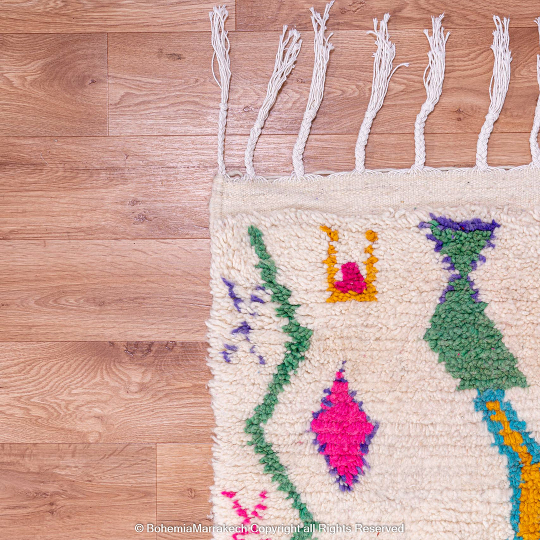 Colorful Azilal Moroccan rug with Berber motifs, handwoven wool art featuring vibrant patterns on a natural background, on wooden floor.