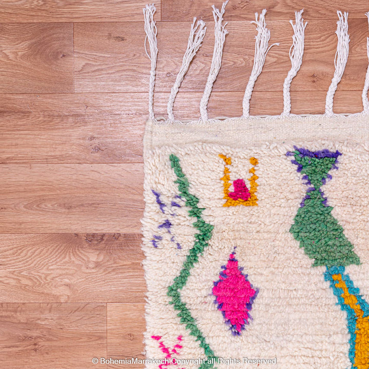 Colorful Azilal Moroccan rug with Berber motifs, handwoven wool art featuring vibrant patterns on a natural background, on wooden floor.