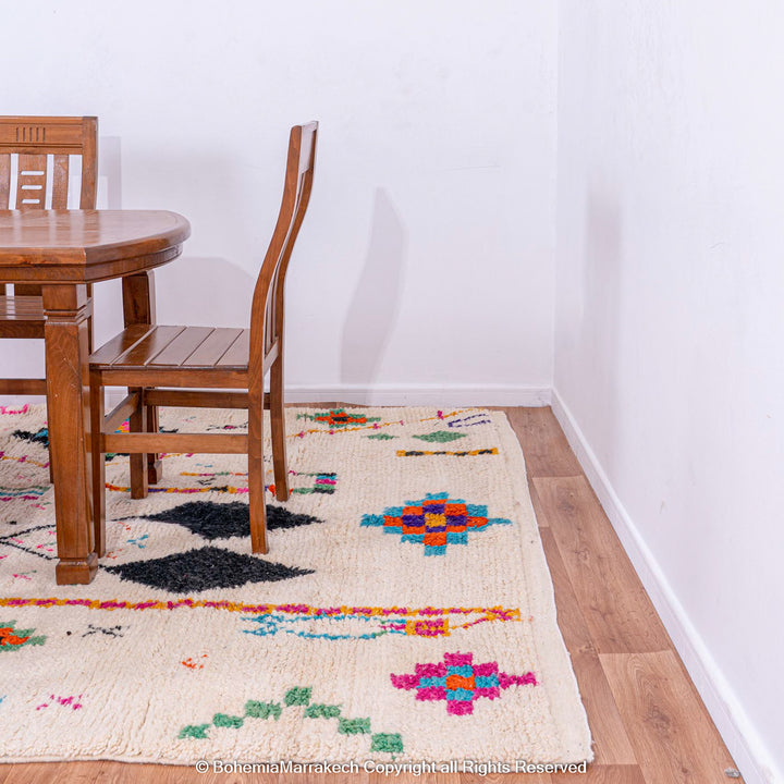 Colorful Azilal Moroccan Rug beneath dining table, showcasing vibrant Berber motifs, handwoven wool from the Atlas Mountains.