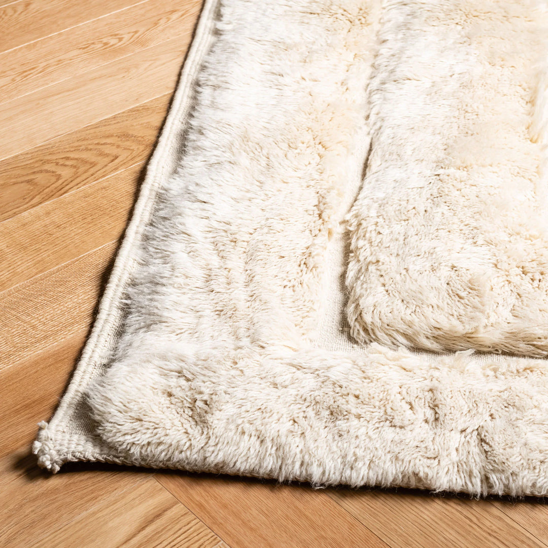 Close-up of cream geometric Beni Mrirt rug on wooden floor, showcasing plush texture and intricate Moroccan design pattern.