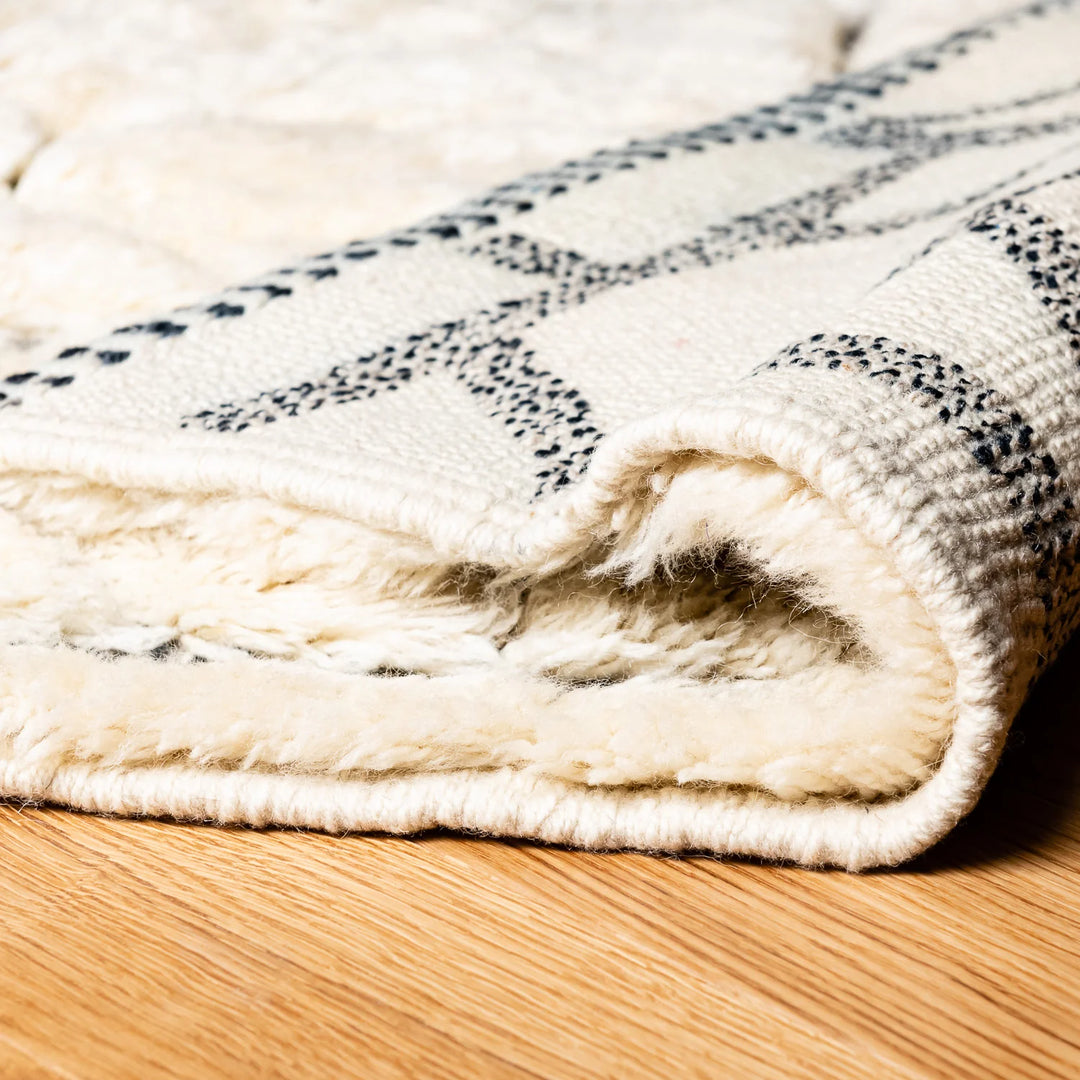 Cream Moroccan wool rug with abstract black grid lines, showcasing plush texture and traditional handmade design on a wooden floor.