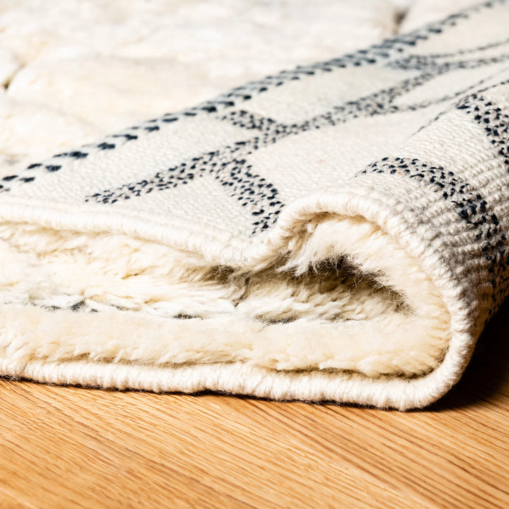 Cream Moroccan wool rug with abstract black grid lines, showcasing plush texture and traditional handmade design on a wooden floor.