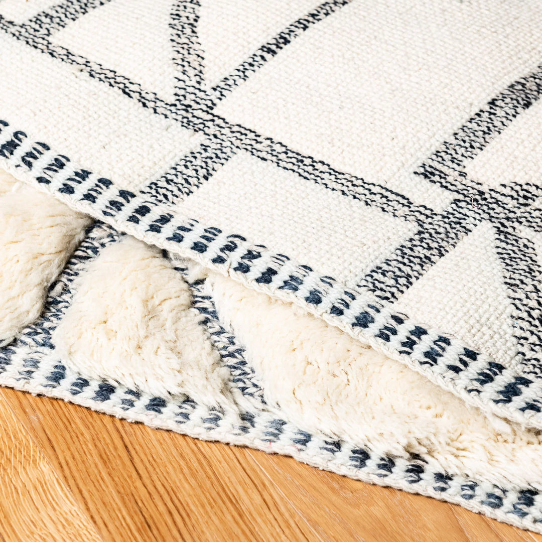 Close-up of a handmade Moroccan wool rug with abstract grid pattern, showcasing plush texture and intricate black linework.