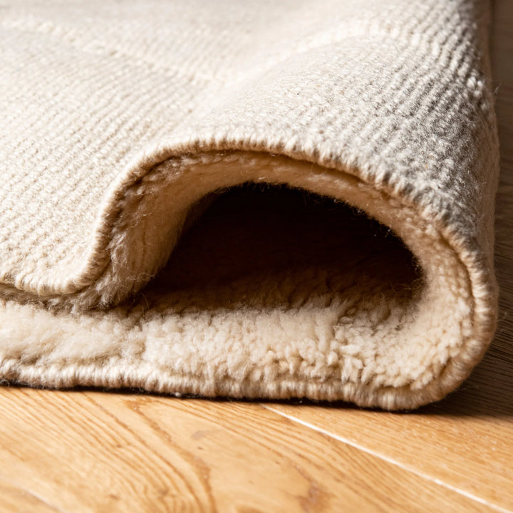 Close-up of cream wool Moroccan rug with subtle raised diamond pattern, handwoven texture on wooden floor.