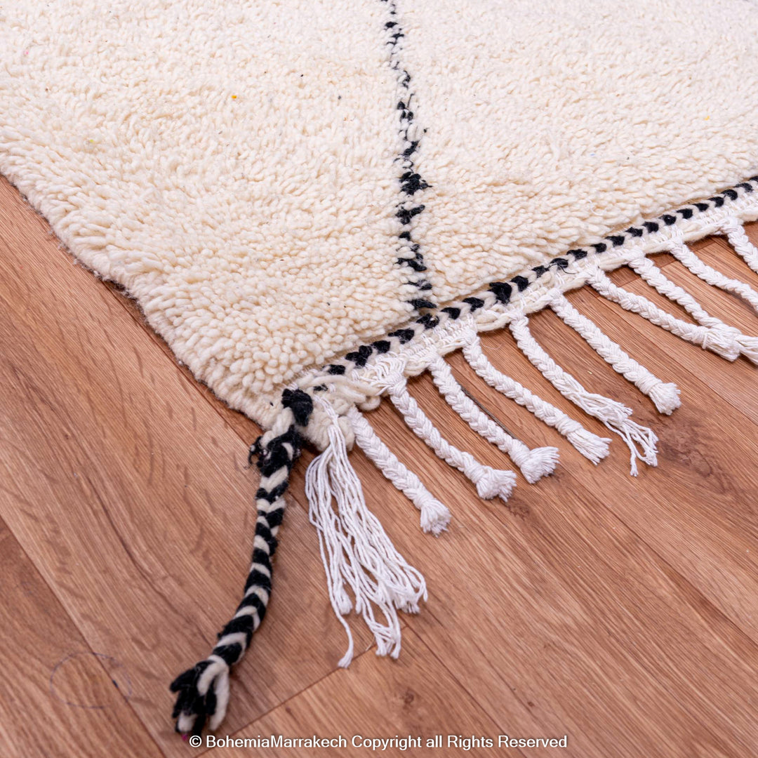 Black and white Moroccan wool rug corner with tassels, showcasing handcrafted Berber design and natural textures on wooden floor.