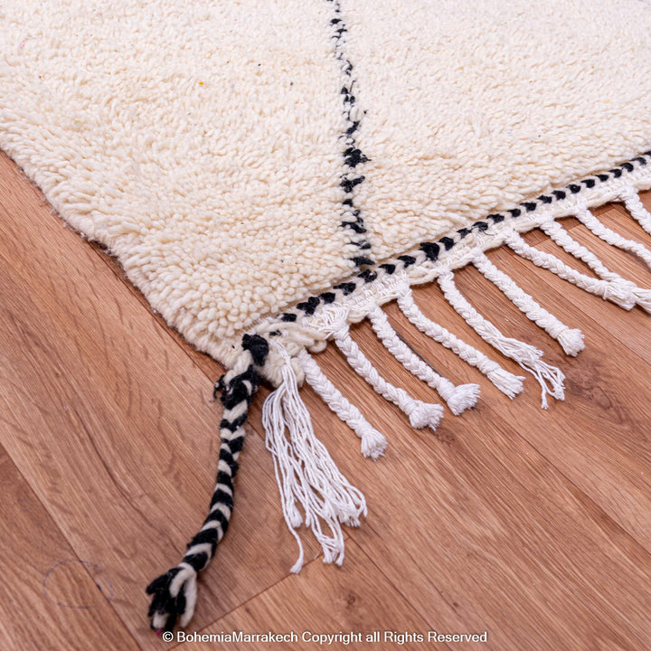 Black and white Moroccan wool rug corner with tassels, showcasing handcrafted Berber design and natural textures on wooden floor.