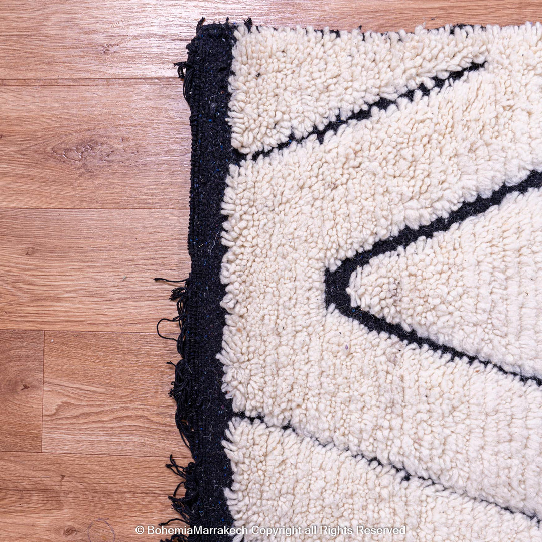 Black and white Moroccan wool rug with diamond pattern on wood floor, traditional Berber design.