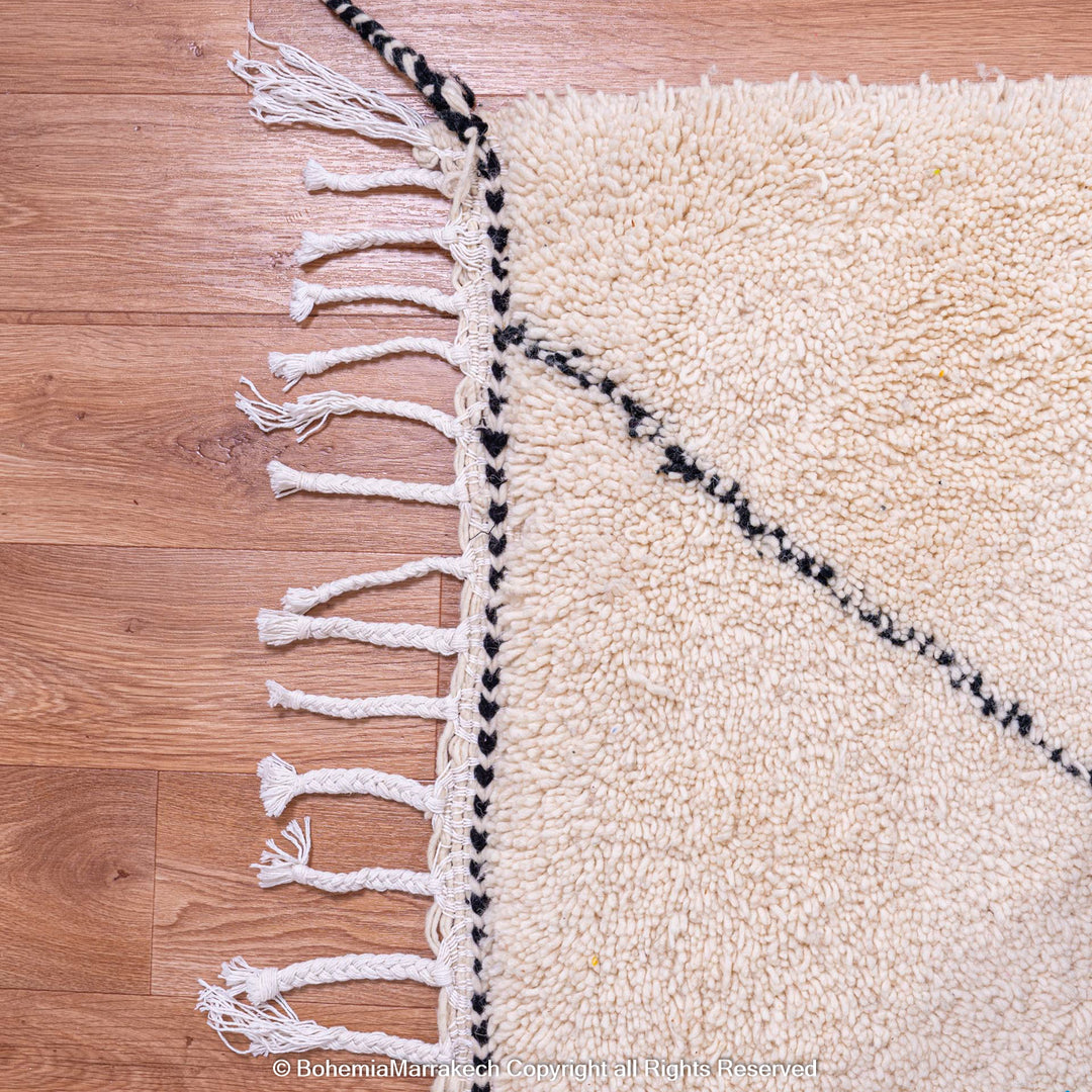 Black and white diamond Moroccan Berber wool rug with lattice pattern and fringe detail on wooden floor.