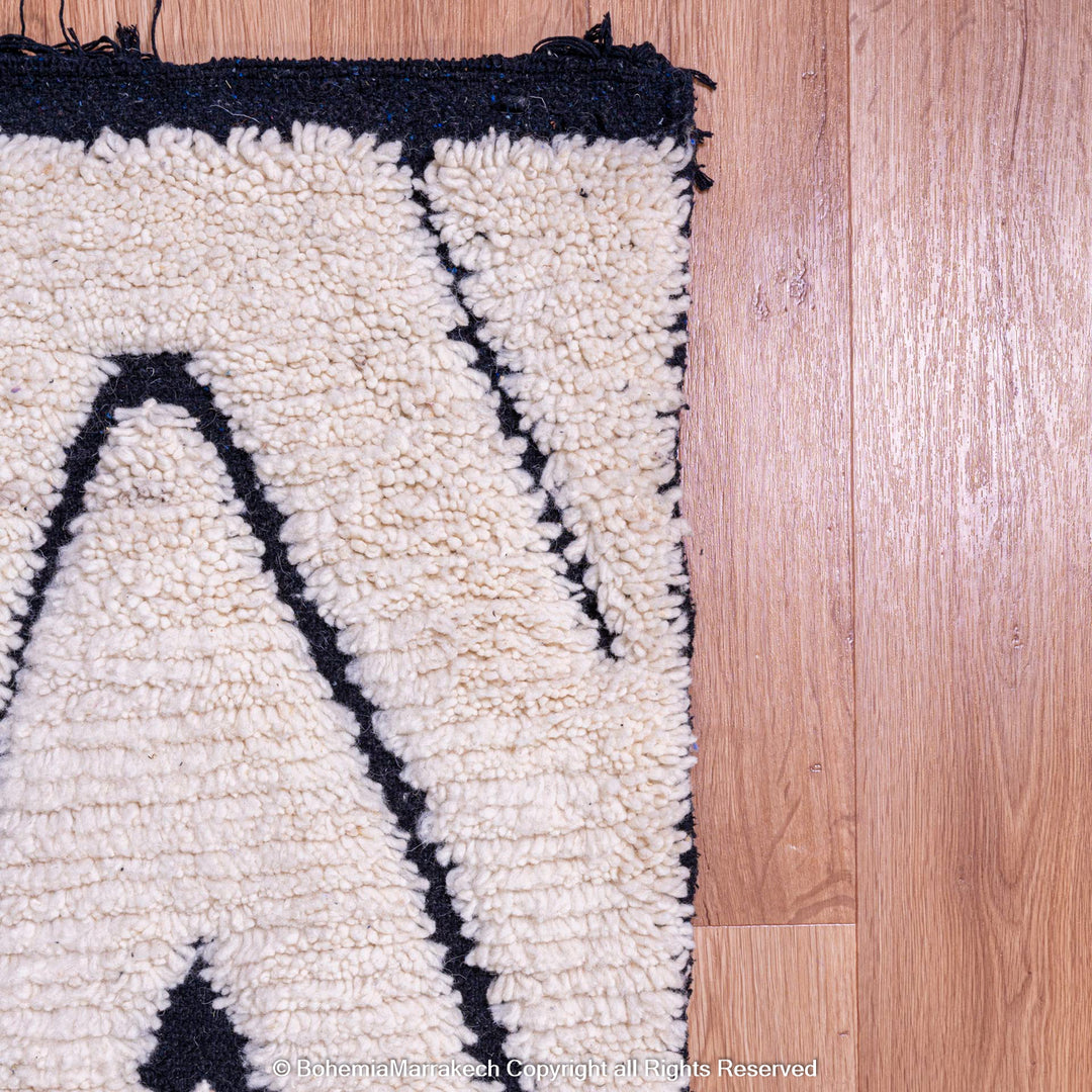 Black and white diamond Moroccan Berber wool rug on wooden floor, showcasing handmade traditional design.